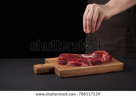 Beef steak and salt by chef on the background with free space for text design or logotype menu restaurant. Food background. Black text area. Copy space
