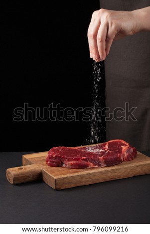 Beef steak and salt by chef on the background with free space for text design or logotype menu restaurant. Vertical photo. Food background. Black text area. Copy space