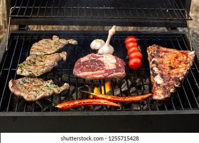 Beef steaks on the grill with flames. On the grill are ribs, steaks and hot peppers.