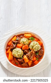 Beef Stew With Dumplings And Vegetables In Rich Tomato And Stock Based Gravy In White Bowl, British Cuisine, Vertical View From Above