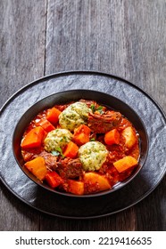 Beef Stew With Dumplings And Vegetables In Rich Tomato And Stock Based Gravy In Black Bowl, British Cuisine, Vertical View From Above, Free Space