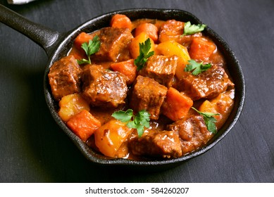 Beef stew in frying pan on black background, close up view