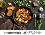 Beef stew with potatoes, carrots and greens in bowl over dark stone background. Comfort healthy food for dinner. Top view, flat lay