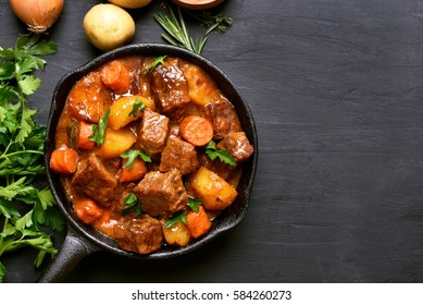 Beef stew with potatoes, carrots and herbs on black background with copy space, top view - Shutterstock ID 584260273