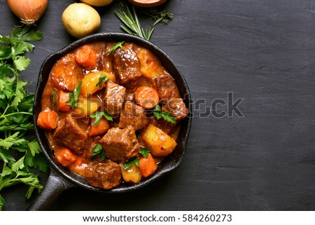 Beef stew with potatoes, carrots and herbs on black background with copy space, top view