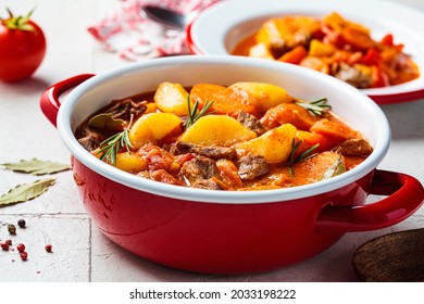Beef stew with potatoes and carrots in tomato sauce in red pot, gray  background. Slow cooking concept. - Shutterstock ID 2033198222