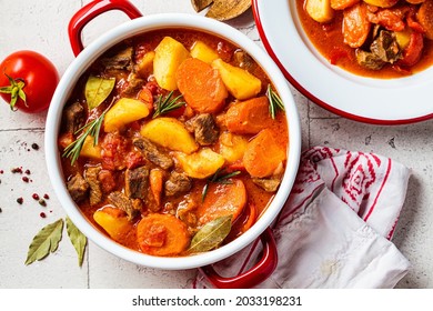 Beef stew with potatoes and carrots in tomato sauce in red pot, gray  background, top view. Slow cooking concept.