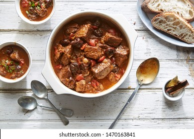 Beef Stew with prunes and vegetables in a pot with bread on a wooden rustic table