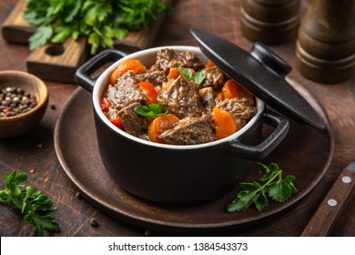 beef stew with vegetables in black pot on dark wooden background, selective focus