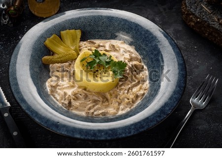 beef stroganoff with mashed potatoes and pickled cucumbers on a dark background
