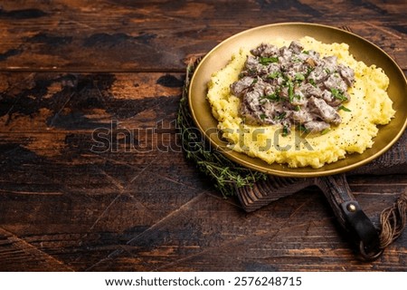 Beef Stroganoff over mashed potatoes with creamy sauce in a plate. wooden background. top view.
