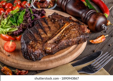 Beef T-Bone steak, herbs and spices on a dark table. Top view. Free space for your text.