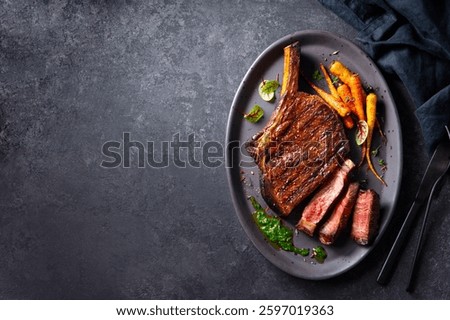 Beef tomahawk steak on a bone with roasted colorful carrots and chimichurri sauce on a plate. Dark grey background. Copy space. Top view.