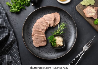 Beef tongue served horseradish sauce and rosemary sprig on black table. Juicy tender meat a great appetizer. Top view.