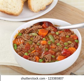 Beef And Vegetable Soup In A White Bowl With Sliced Bread In Background