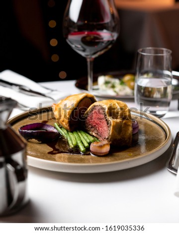 Beef wellington with a glass of red wine on a white tablecloth at a restaurant