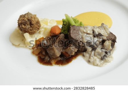 A beef-based main course featuring cubed meat cooked to well-done, artfully plated and accompanied by vegetables.