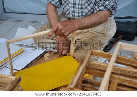 Beekeeper making frames for bee hives by pressing the beeswax foundation onto the frame using a wooden tool outside a shop on Seydikemer high street