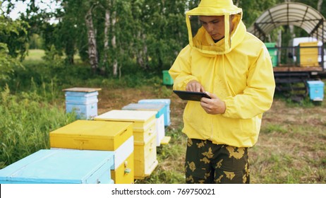 Beekeeper Man With Tablet Computer Checking Wooden Beehives Before Harvesting Honey In Apiary