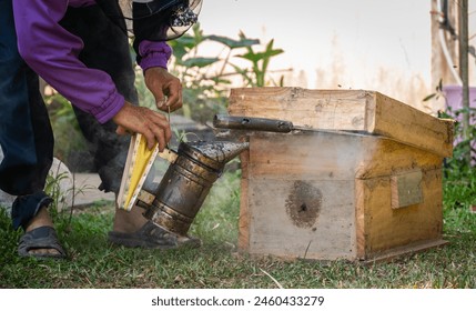 Beekeeper using smoker to calm the bees while inspects them or works around the hive. Smoking a beehive masks this pheromone, allowing the beekeeper to safely perform a hive inspection. - Powered by Shutterstock