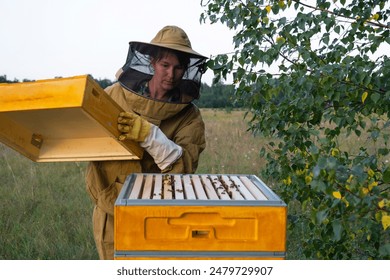 A beekeeper, a woman in a protective suit against bee stings, holds a frame with honey from a bee hive in her hands. Beekeeping, care of the hive - Powered by Shutterstock