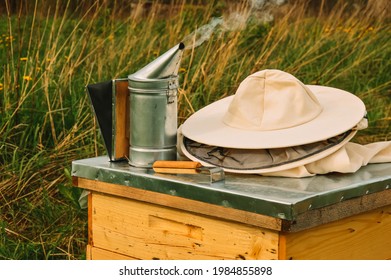The beekeeper's tools are lying on the hive. Smoker, chisel and protective equipment of the beekeeper on the bee house. Apiary in nature. Honey production. Bees. Natural healthy honey.