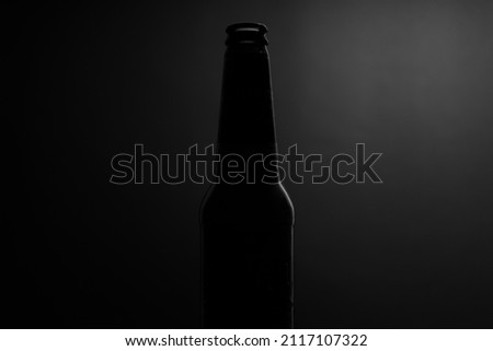Beer bottle against a dark black moody background with a rim light.