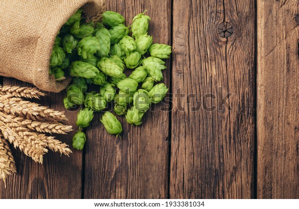 Beer\
brewing ingredients, hops, and wheat ears on a wooden cracked old\
table. Beer brewery concept. Hop cones and wheat closeup. Sack of\
hops and sheaf of wheat on vintage\
background.