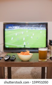 Beer, Chips And Remote Controls On The Table (in The Background TV - Football Game)