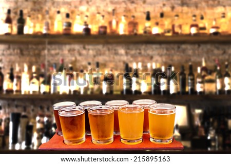 Beer flight of eight sampling glasses of craft beer on a bar countertop.