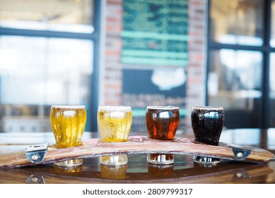 Beer flight with four craft beer samples served on a wooden tasting paddle in a brewery taproom with blurred background.