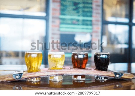 Beer flight with four craft beer samples served on a wooden tasting paddle in a brewery taproom with blurred background.
