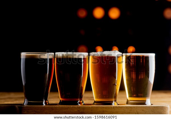 Beer flight. Traditional classical American diner or bar\
drink item with variety of beers for tasting. IPA, wheat beer,\
porter, Pilsner, pale ale, stout. Lined up on the bar at a\
restaurant. 