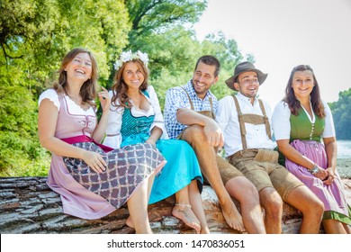  Beer garden in Bavaria, Germany - friends in Tracht, Dirndl and Lederhosen.Five friends having fun on Bavarian River and clinking glasses with beer.Oktoberfest