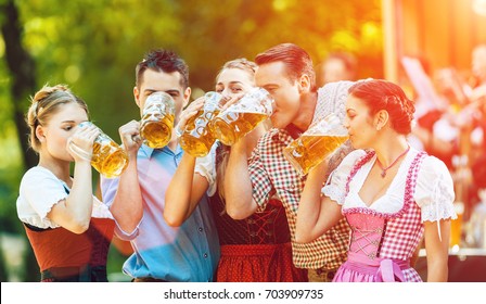 Im Biergarten in Bayern, Deutschland - Freunde in Tracht, Dirndl und Lederhosen und Dirndl stehen vor der Band