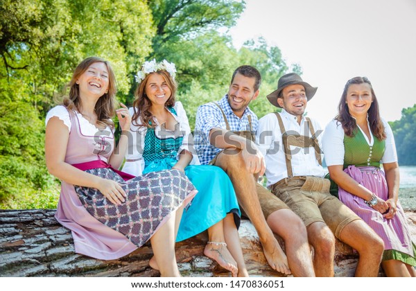  Beer garden in Bavaria,\
Germany - friends in Tracht, Dirndl and Lederhosen.Five friends\
having fun on Bavarian River and clinking glasses with\
beer.Oktoberfest