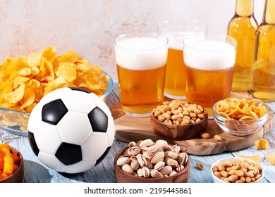 Beer In Glasses And Snack On Wooden Table With Football Ball, Football Game Night Food. Snack And Drink For Watching Football Games And Championships