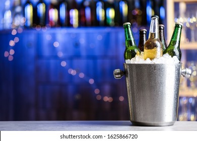 Beer in metal bucket with ice on table against blurred lights - Powered by Shutterstock