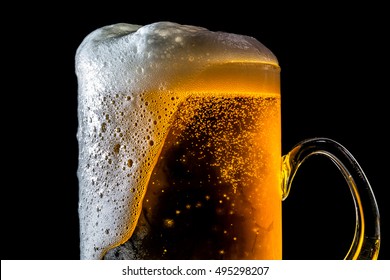 Beer Overflowing Large Glass With Foam And Bubbles Isolated On A Black Background
