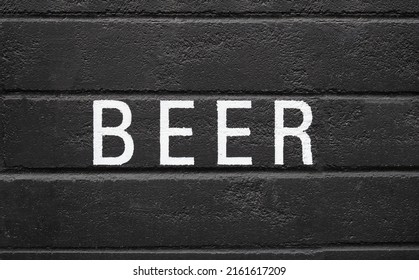 Beer painted on black concrete wall. White capital letters on black surface. Alcoholic beverage or drink advertisement backdrop. Pub, bar, restaurant or wine store background texture or signage. 