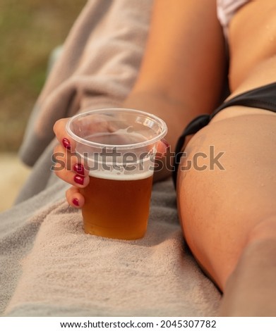 Beer in a plastic glass in the hand of a girl on the beach.