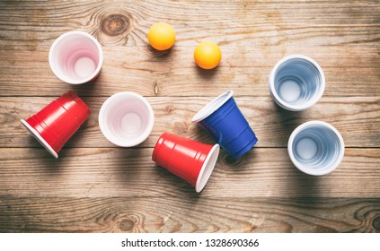 Beer Pong, College Party Game. Plastic Red And Blue Color Cups And Ping Pong Balls On Wooden Background, Top View