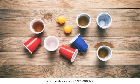 Beer Pong, College Party Game. Plastic Red And Blue Color Cups And Ping Pong Balls On Wooden Background, Top View