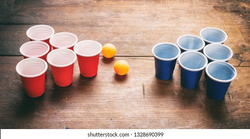 Beer Pong, College Party Game. Plastic Red And Blue Color Cups And Ping Pong Balls On Wooden Background, View From Above