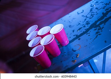 Beer Pong Playing At A Party, American Red Cups Standing On A Textured Wet Table Night Club 