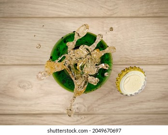 Beer Popping And Splash From A Green Bottle On Wooden Background, Top View