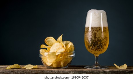 Beer and Potatoes Chips. Glass of blonde beer with a large head of foam. Chips in glass bowl good for snack on natural wooden table. Good for beer festival, pub, restaurant advertising. Food and Drink - Powered by Shutterstock
