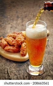 beer pouring into glass and fried chicken wings on wooden table