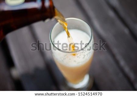 Beer pouring out with top view. Liquid pouring from the bottle into the glass leaving it full. Wood background.