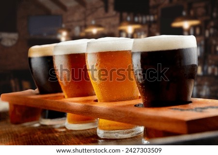 Beer samplers in small glasses individually placed in holes fashioned into a unique wooden tray. Focus is on the backlit light beers, featuring some residual effervescence.
